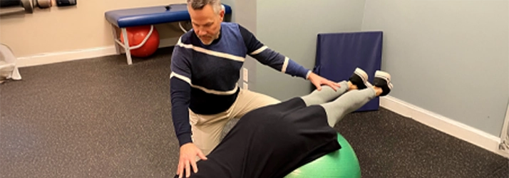Dr. Andrew Knecht in a physical rehabilitation session with a patient lying on an exercise ball.