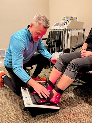 Dr. Andrew Knecht using a red light therapy device on a patient’s feet.